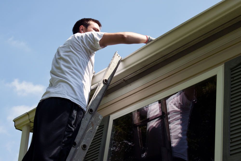 Young-man-on-latter-cleaning-house-gutters